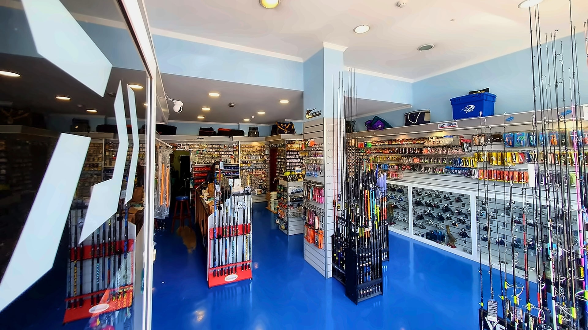 Inside O Inglês - Pesca Desportiva in São Martinho, Funchal: rods, reels and lures over the bright blue floor.
